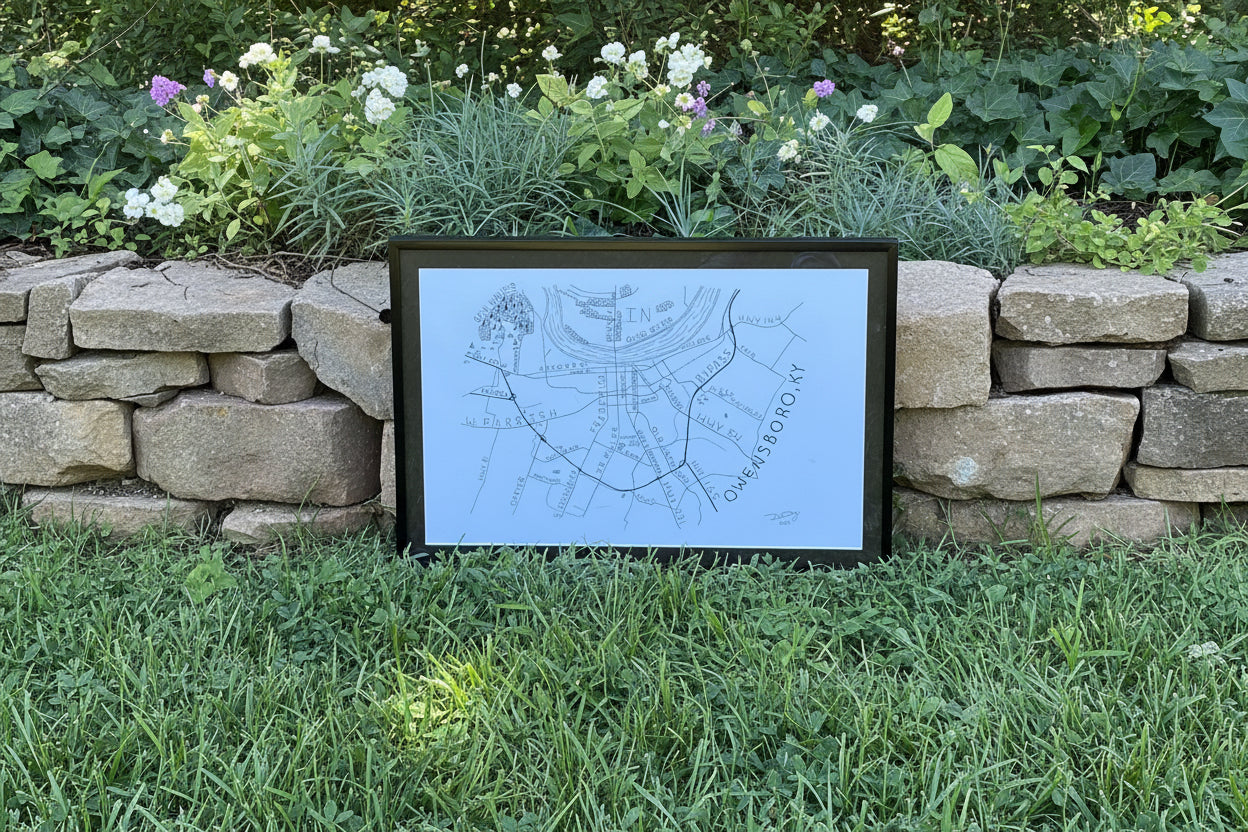 Framed Owensboro Kentucky map artwork by Dexter Day displayed outdoors in a natural garden setting