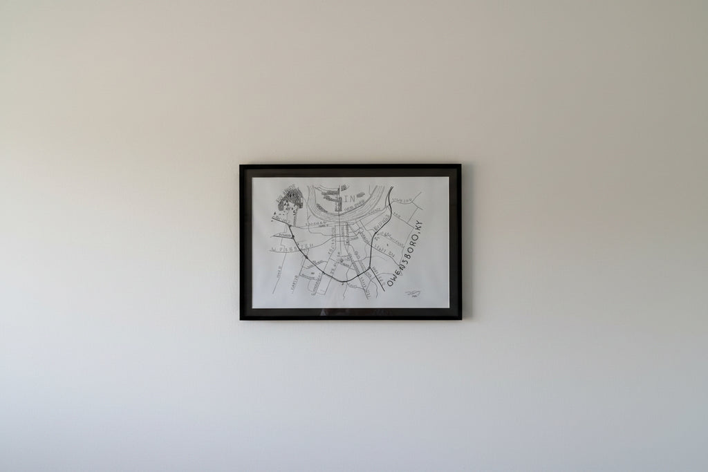 Framed hand-drawn Owensboro Kentucky map by artist Dexter Day displayed on a wall showing size and real-world presentation
