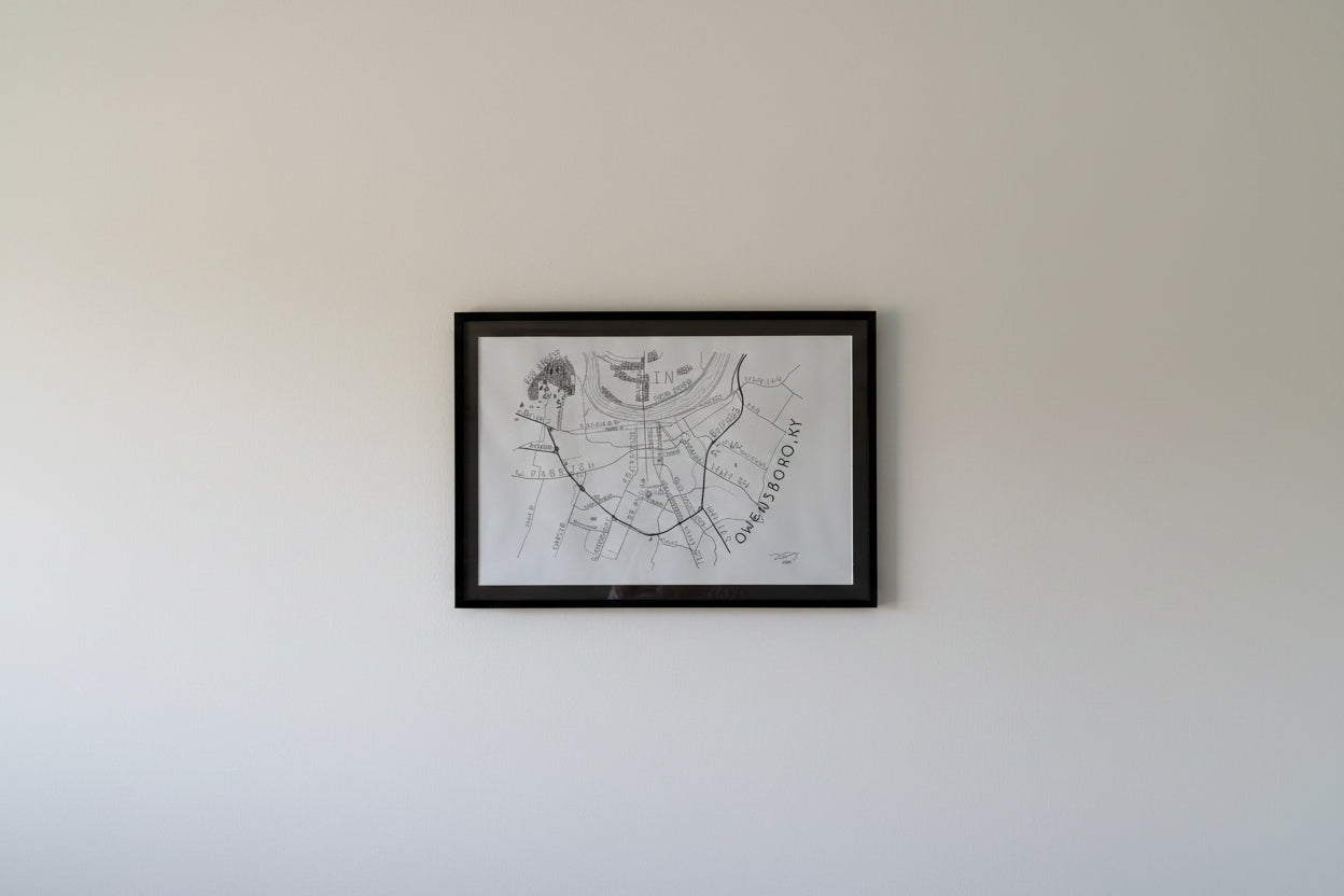 Framed hand-drawn Owensboro Kentucky map by artist Dexter Day displayed on a wall showing size and real-world presentation